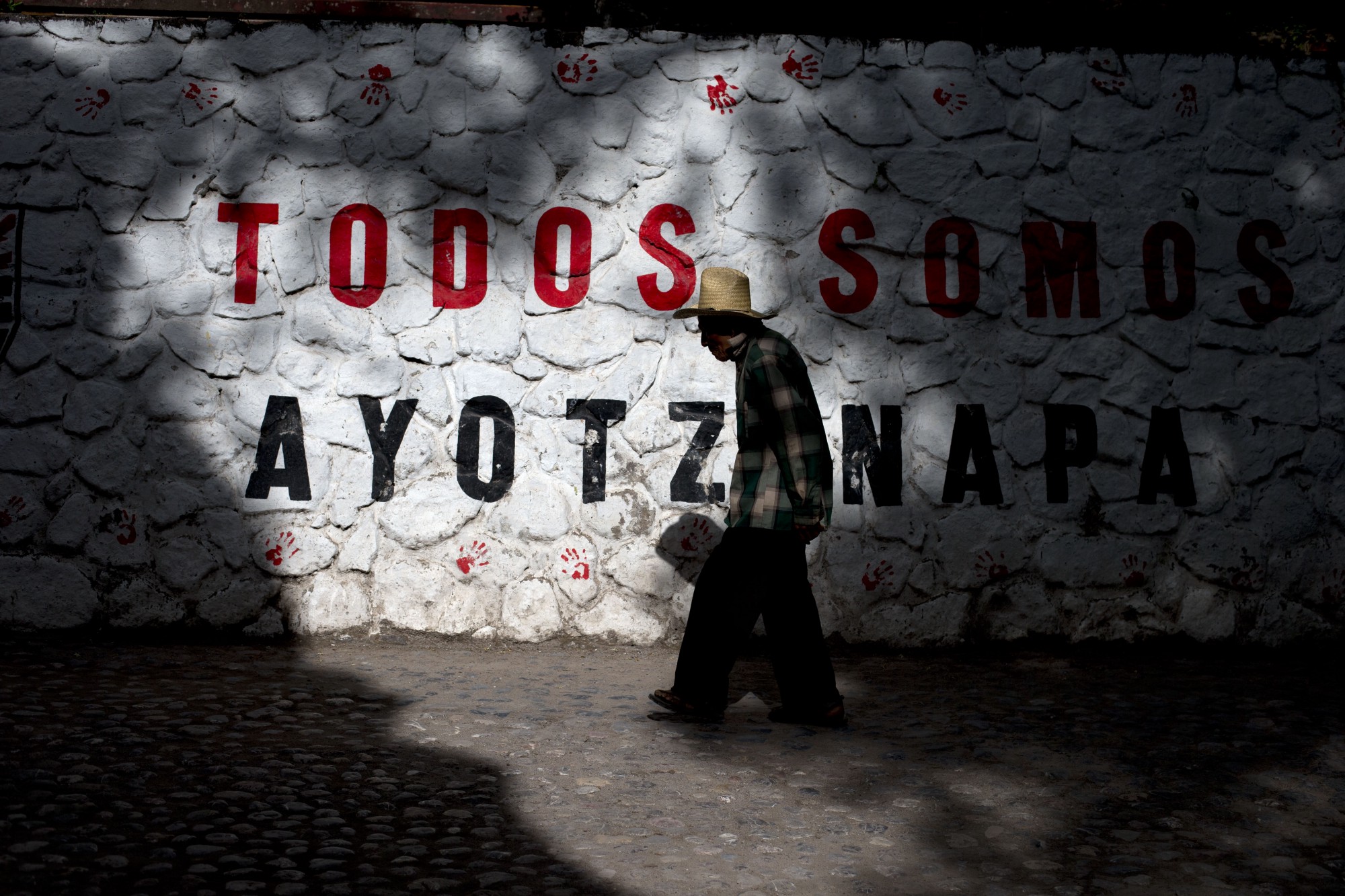 Un año después de la desaparición, un hombre pasa junto a un muro donde se lee “Todos somos Ayotzinapa”.