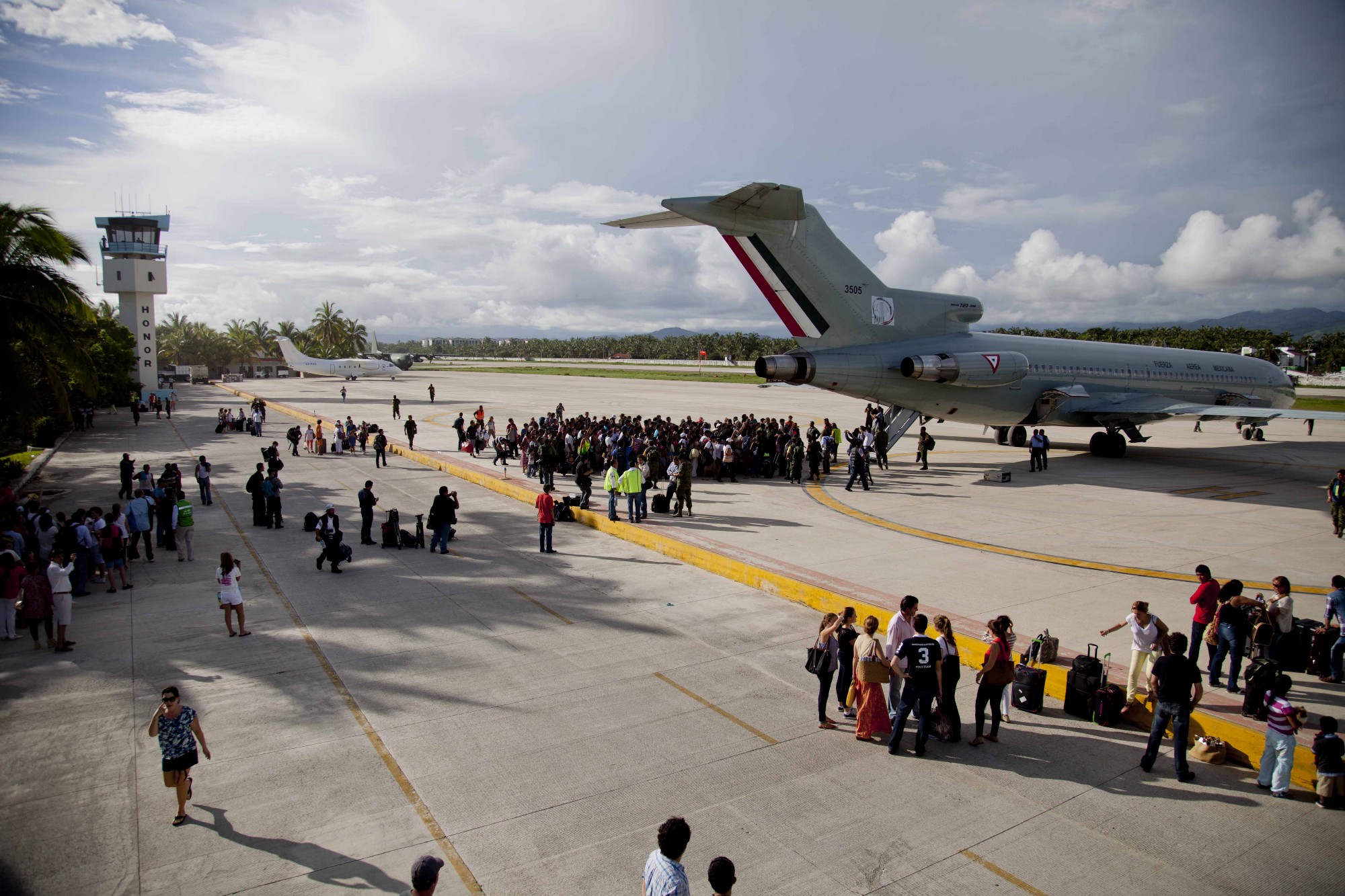 Cientos de turistas se reúnen afuera de un avión de la Fuerza Aérea Mexicana para ser evacuados en la base Pie de la Cuesta, cerca de Acapulco tras una tormenta tropical en el año 2013.