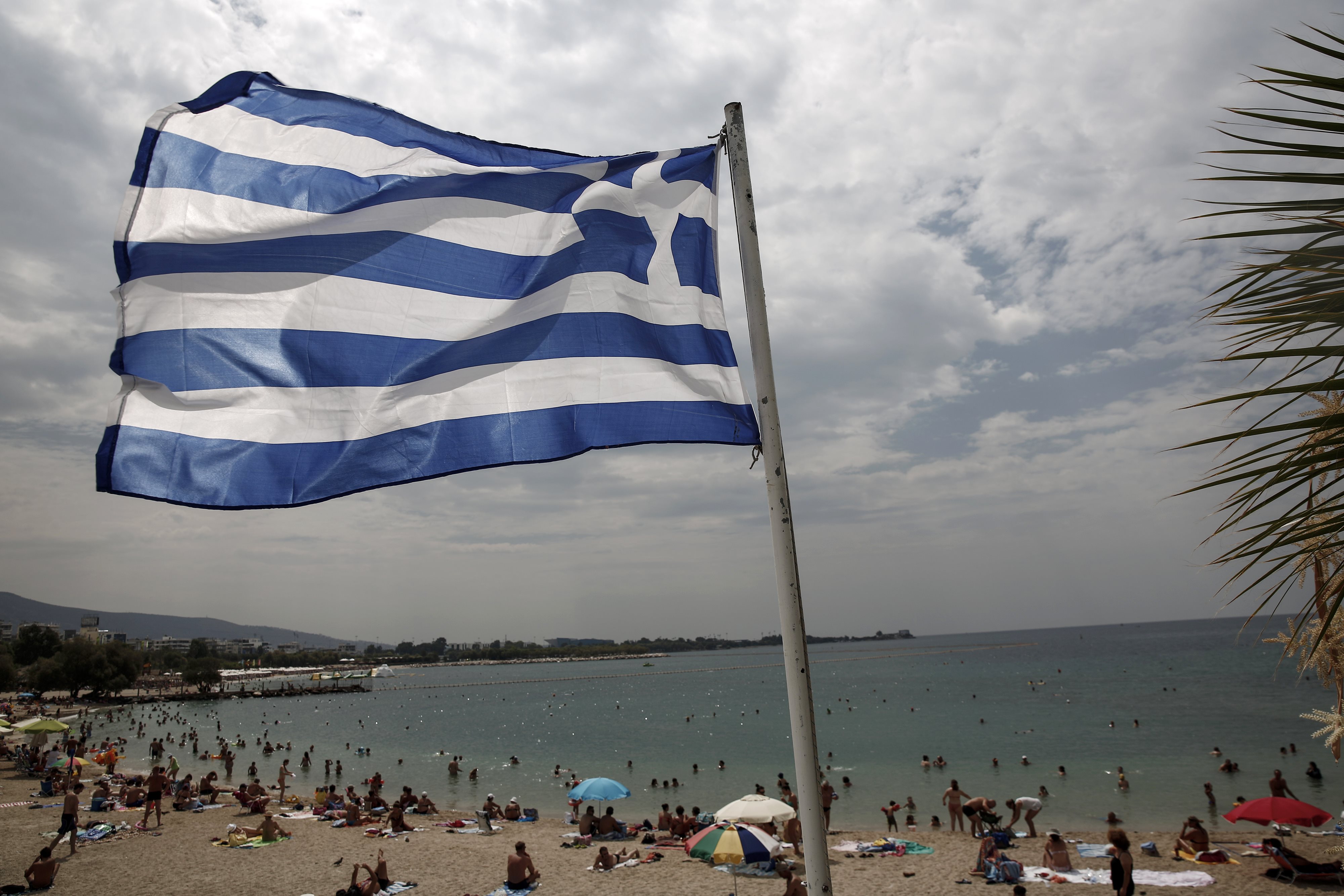 Vista de una bandera griega frente a una concurrida playa en un suburbio de Atenas, Grecia (AP)