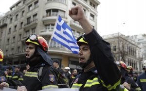 Bomberos cantan lemas frente a una bandera griega durante una protesta en el centro de Atenas, para exigir mejores condiciones de contratación (AP)
