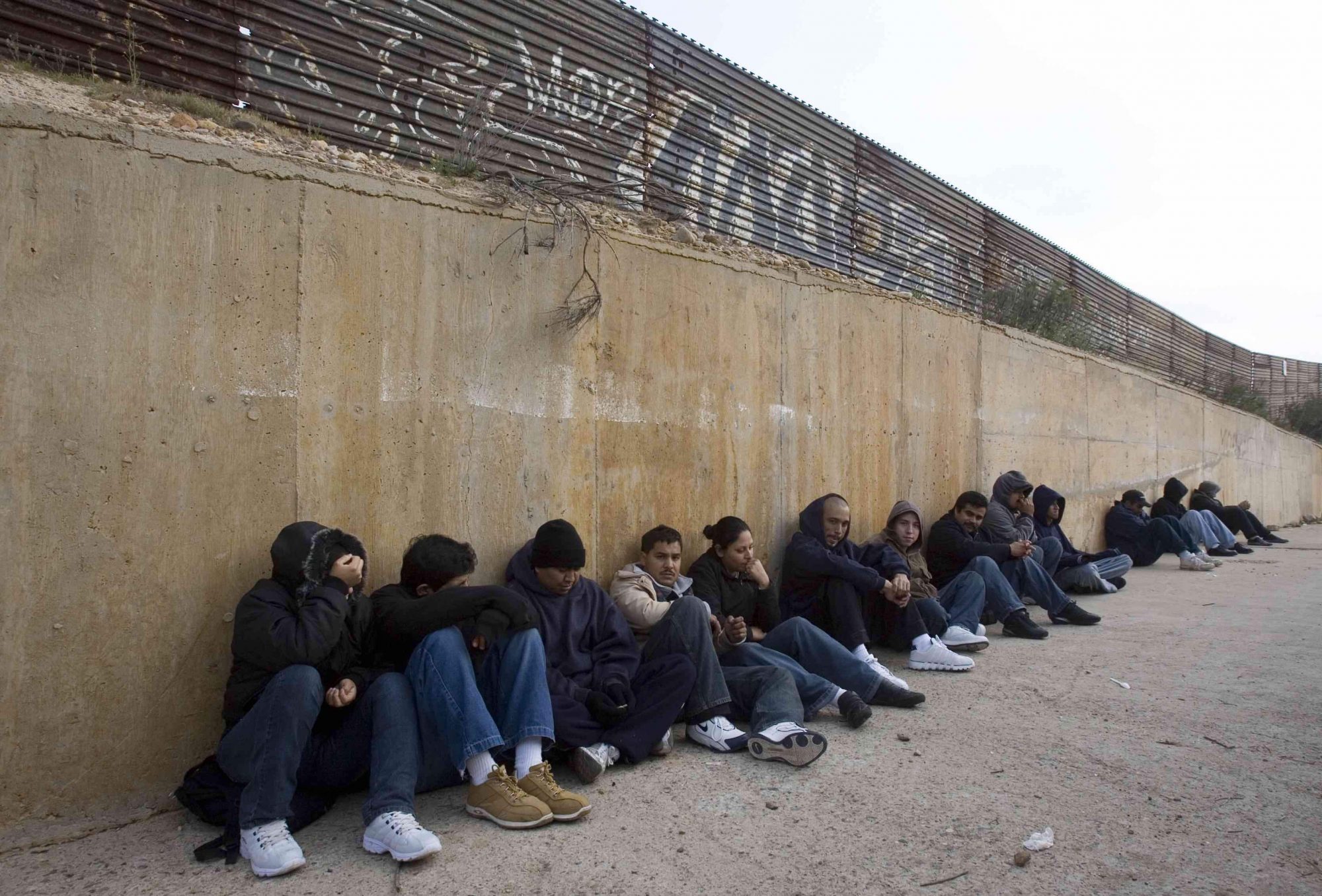 En esta foto de 2008, migrantes esperan junto a la barda fronteriza de Tijuana para cruzar por la noche.