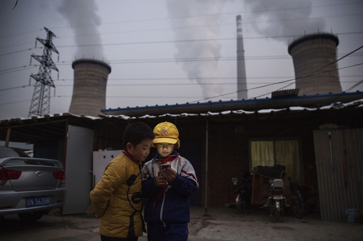 Niños chinos miran su smartphone delante de su casa al lado de una central eléctrica (Getty Images)