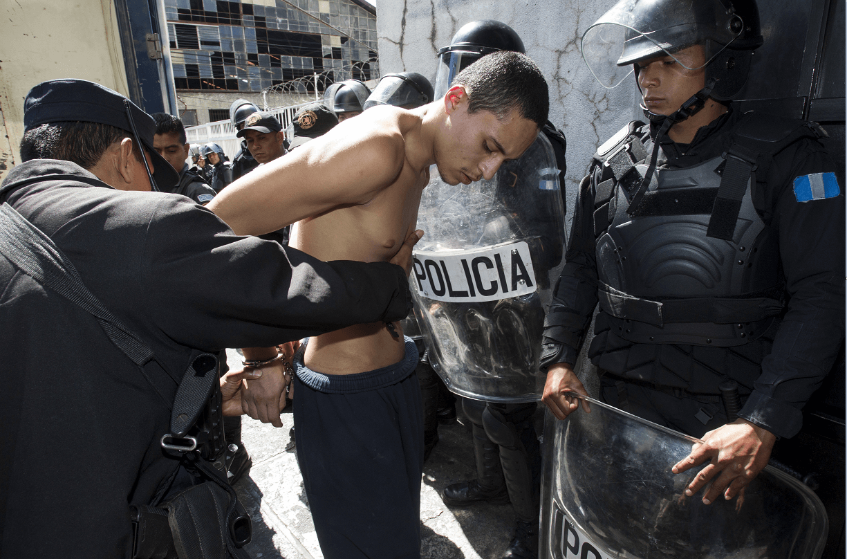 Un policía de Guatemala catea a un miembro de la pandilla Barrio 18 que participó en el motín. (AP)
