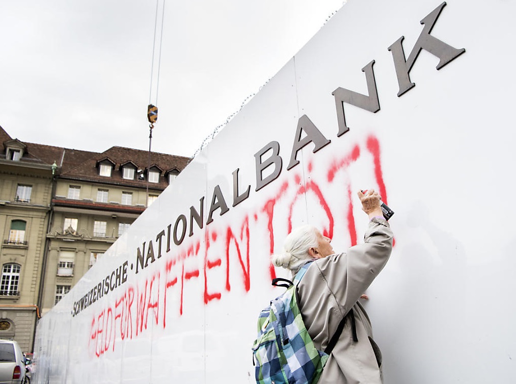 La activista de 86 años Louise Schneider pinta el lema: "El dinero para armas mata" en una pared del Banco Nacional de Suiza (Foto: luzernerzeitung.ch)