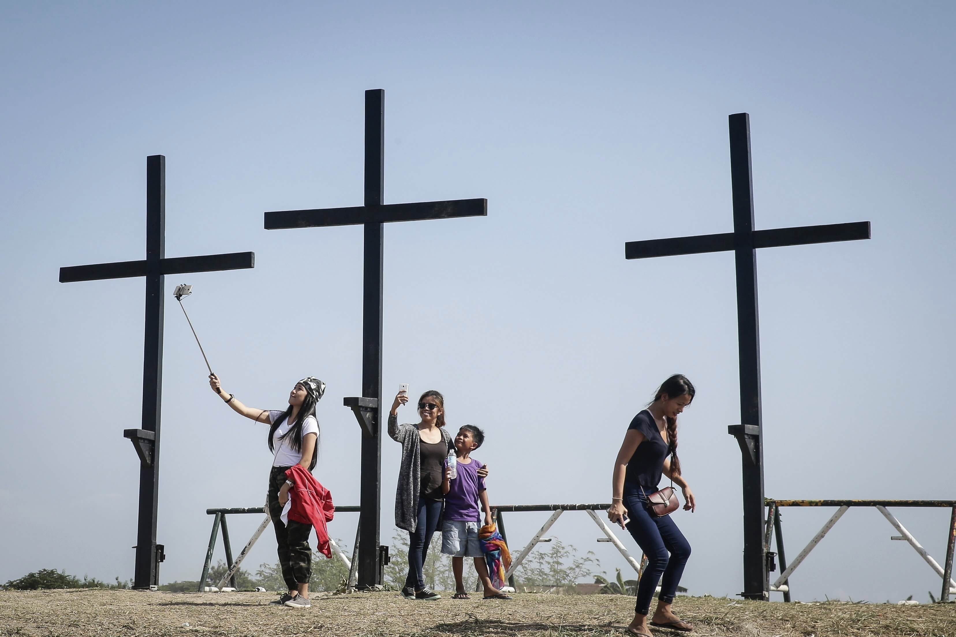 Turistas se hacen fotos junto a tres cruces tras la representación de la crucifixión de Cristo con motivo de la celebración del Viernes Santo en San Fernando, Filipinas (EFE)