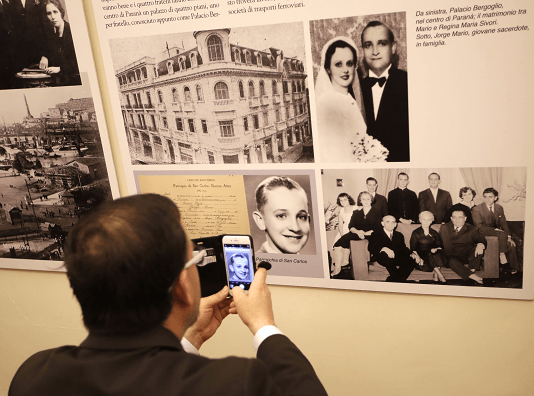 Un hombre que visita la exposición sobre la migración, en Roma, toma una foto de Jorge Bergoglio cuando era niño. (AP)