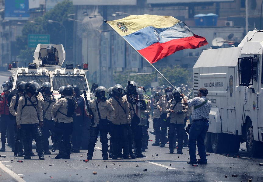 Un partidario de la oposición agita una bandera venezolana frente a la policía antidisturbios durante una manifestación contra el presidente de Venezuela, Nicolás Maduro (Reuters)