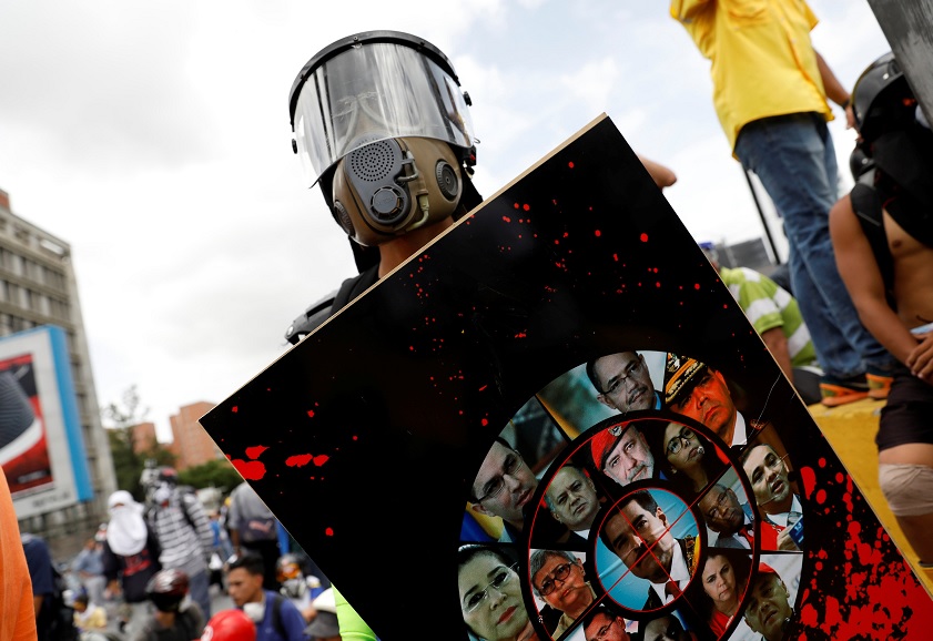 Un manifestante usa un escudo hecho con fotos de políticos de Venezuela (Reuters)