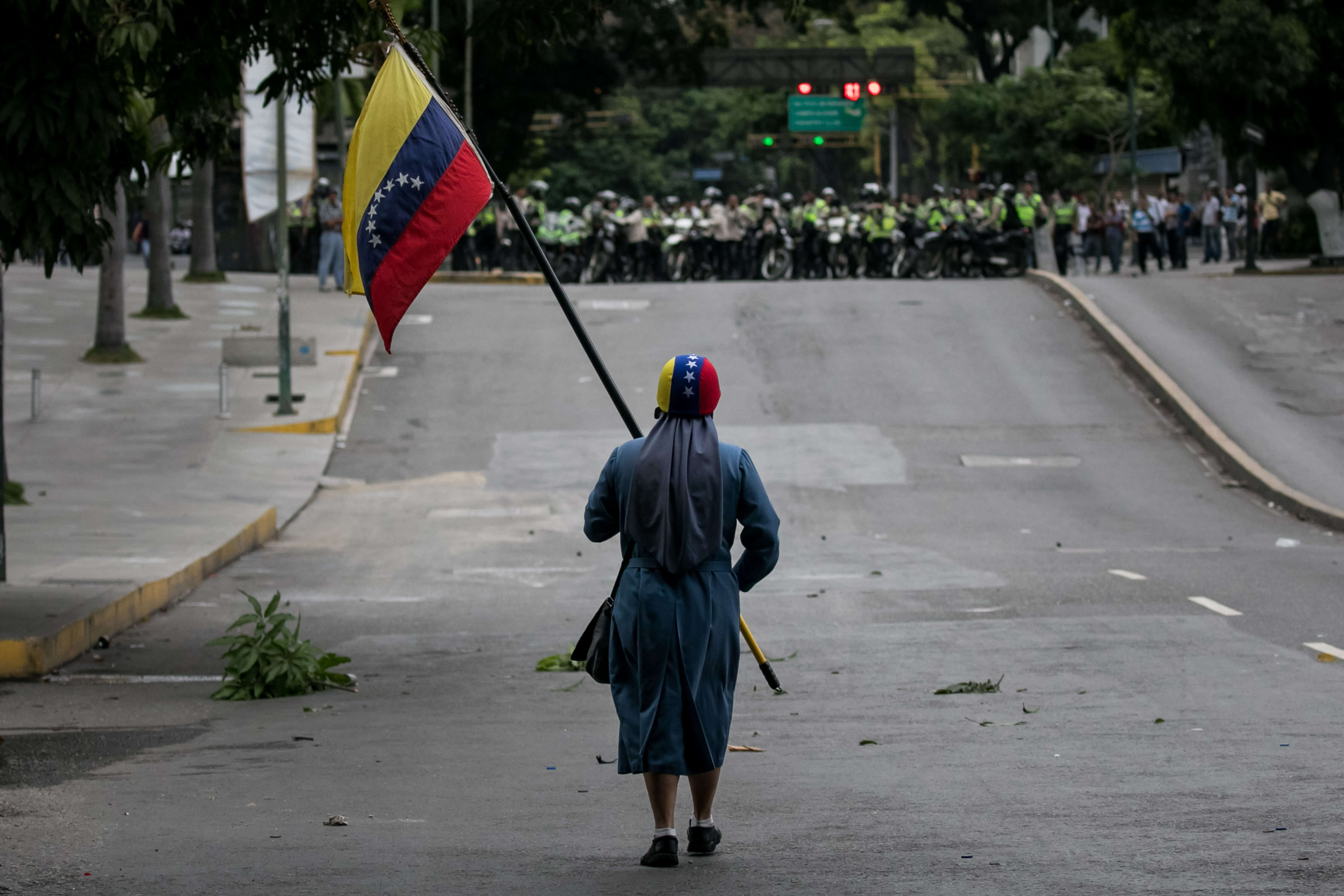 Manifestante ondea bandera de Venezuela frente a columna de policías