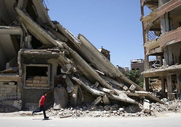 Un joven juega frente a edificios dañados por bombardeos en Damasco (Reuters)