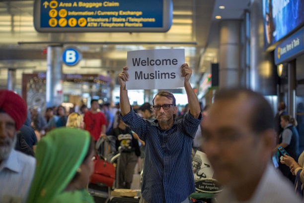 Un hombre lleva una señal de bienvenida a los viajeros que llegan a EU tras las prohibiciones del presidente Trump (Getty Images)