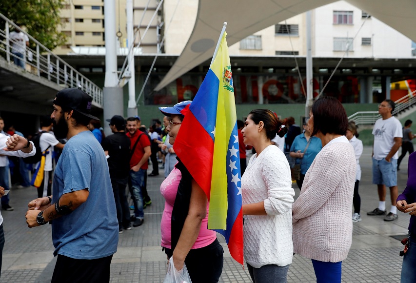 Una mujer sostiene una bandera nacional mientras está en línea junto con otros para emitir su voto durante un plebiscito no oficial contra el gobierno del presidente de Maduro (Reuters)