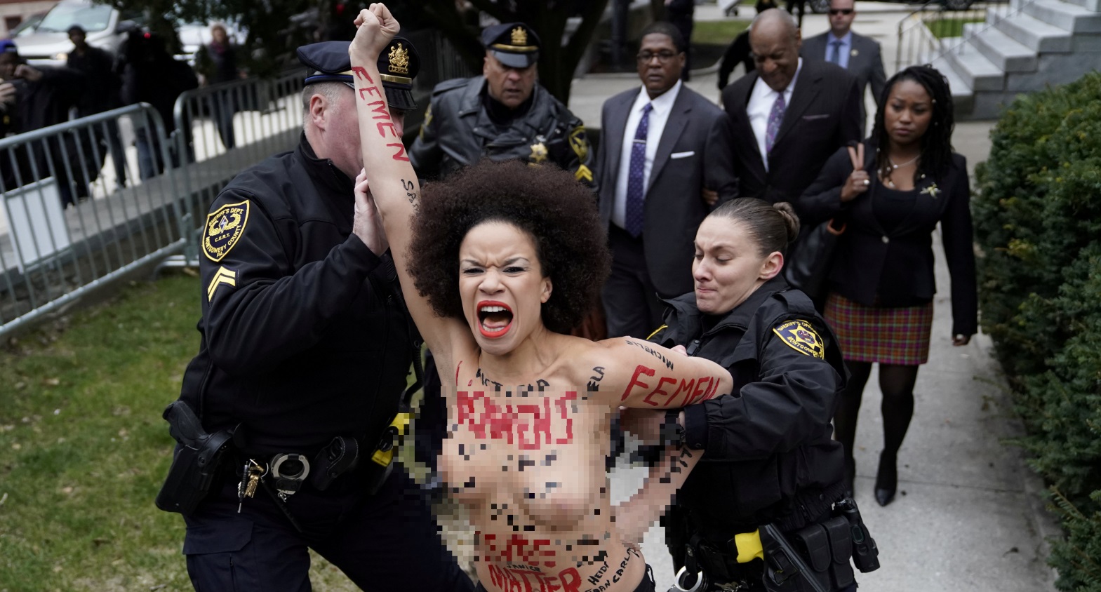 Mujer con torso desnudo protesta frente Bill Cosby en juicio agresión sexual