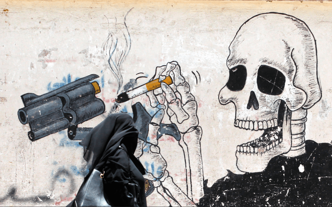 Una mujer en Yemen camina junto a un grafiti en alusión al tabaco. (EFE) 