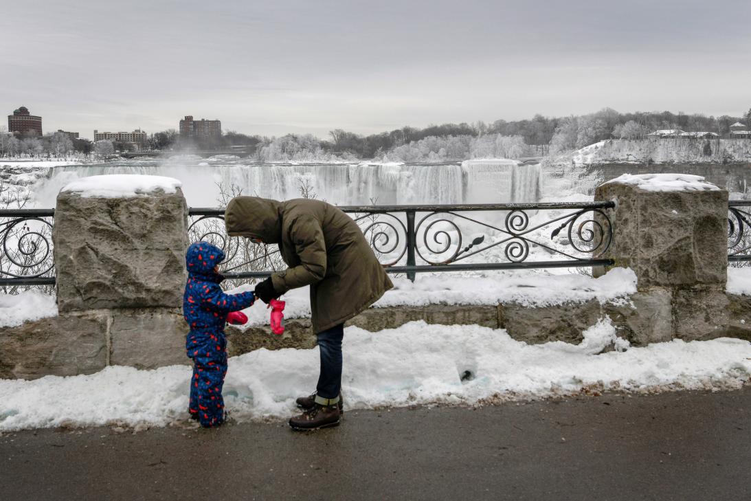 Un padre coloca los guantes de invierno a su hijo, al fondo las cataratas heladas el 22 de enero de 2019. (Reuters)