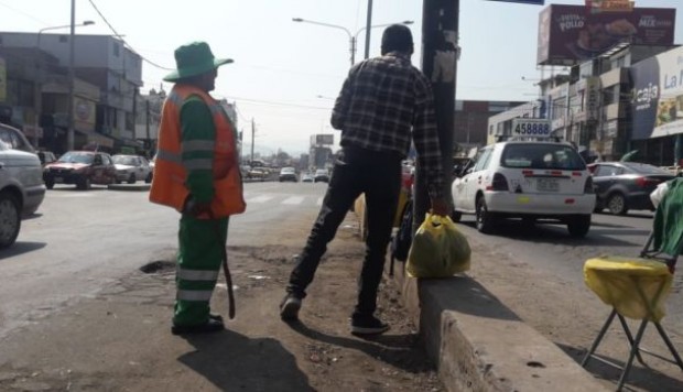 Leonisa Condori vestida con su uniforme de trabajadora de limpieza, convenciendo a un hombre de no tirar basura en la vía, correa en mano (Zenaida Condori/El Comercio)