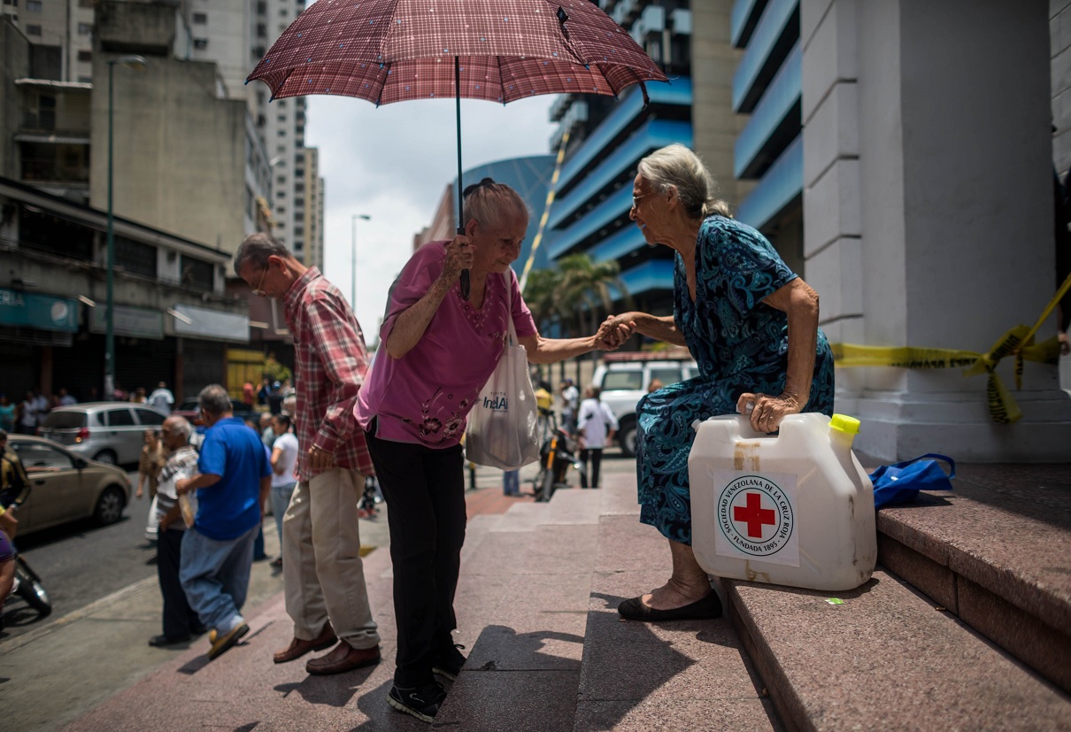 Foto: Dos ancianas cargan un bidón al salir de la sede de la Cruz Roja en Caracas, Venezuela. El 18 de abril de 2019