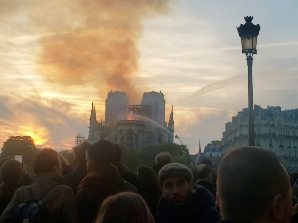 Foto: Las personas se reúnen mientras los bomberos rocían agua para extinguir las llamas mientras la catedral de Notre Dame arde en París, Francia, el 15 de abril de 2019 (Reuters)