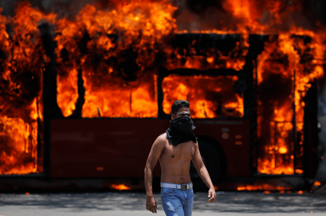 Foto: Opositor venezolano camina frente a autobús incendiado, 30 de abril de 2019, Venezuela