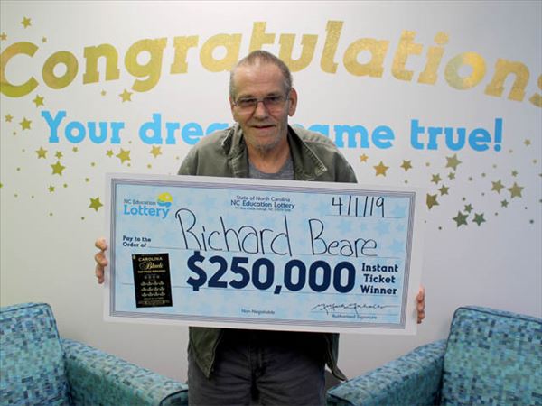 Richard Beare, ganador de la lotería 'scratch-off' en Carolina del Norte, posa frente a la cámara sosteniendo su cheque de 250 mil USD (NCLottery)