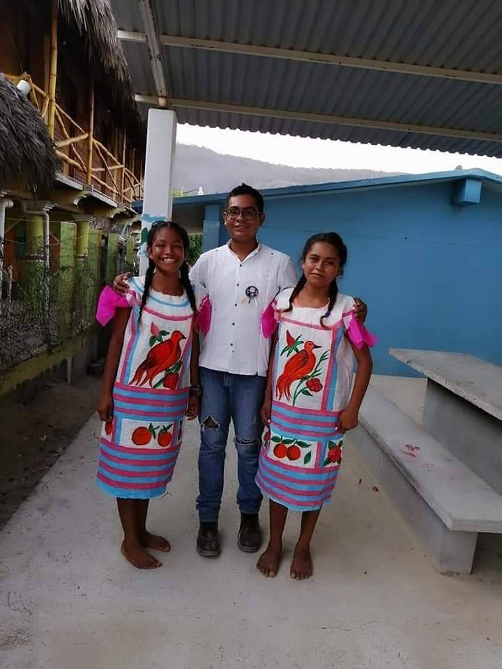 El maestro Armando Reyes posa al centro de la fotografía junto a dos alumnas que están usando sus huipiles hechos a mano (Facebook Cosas de oaxaqueños)