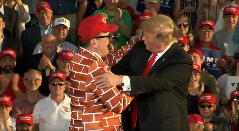 Hombre vestido de muro saluda a Trump en mitin