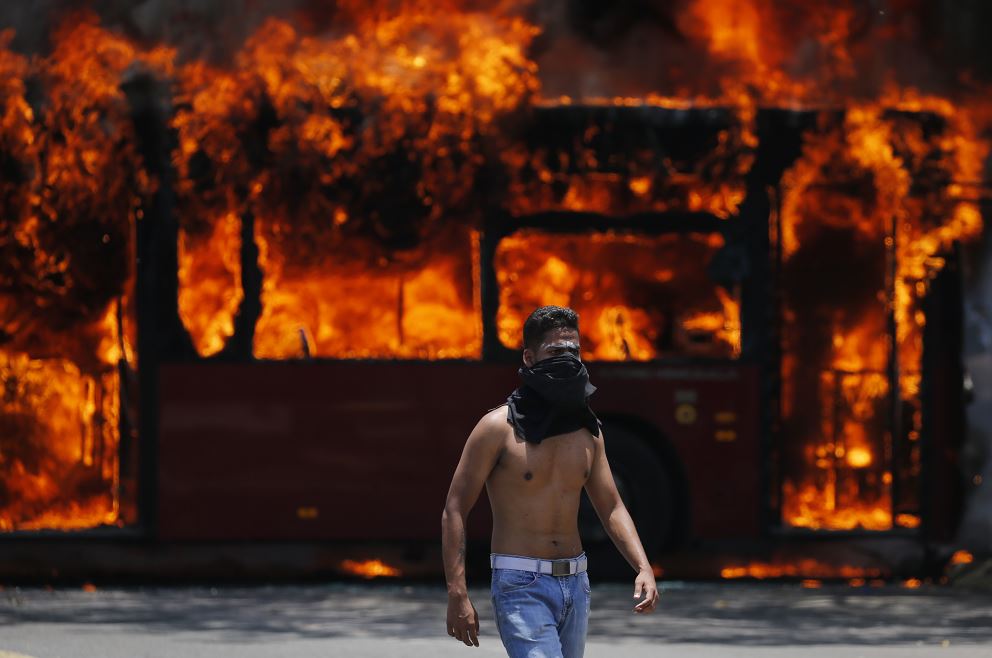 Foto: Un manifestante antigubernamental camina cerca de un autobús incendiado por opositores a Nicolás Maduro, 1 mayo 2019