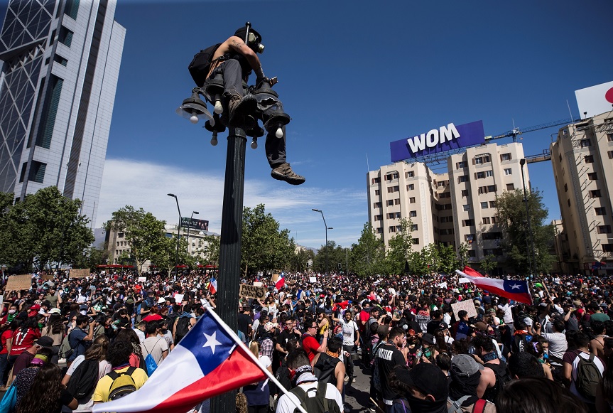 Foto: Un joven toma fotografías de la protesta en Santiago arriba de un poste. Efe