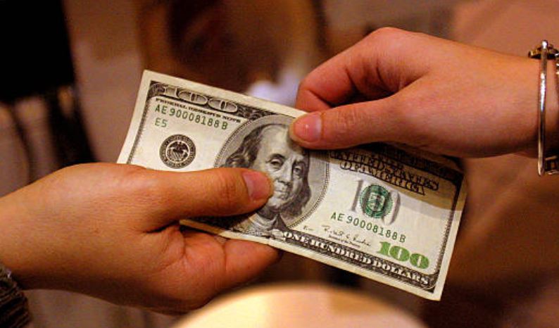 Foto: Dos personas sostienen con su manos un billete de 100 dolares, 21 noviembre 2019
