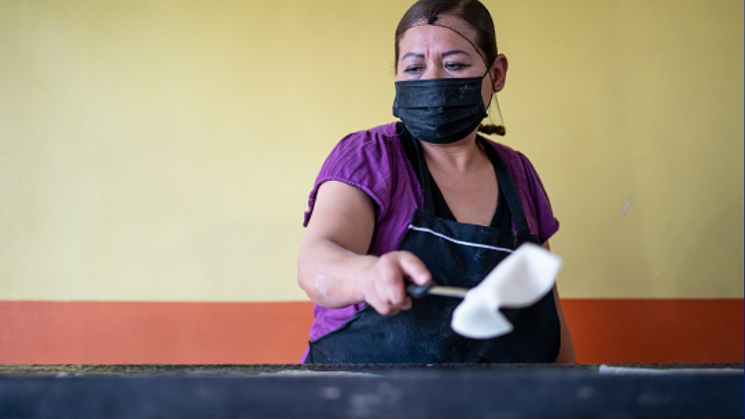 Foto: Una señora usa cubreboca mietras hace tortillas. Getty Images
