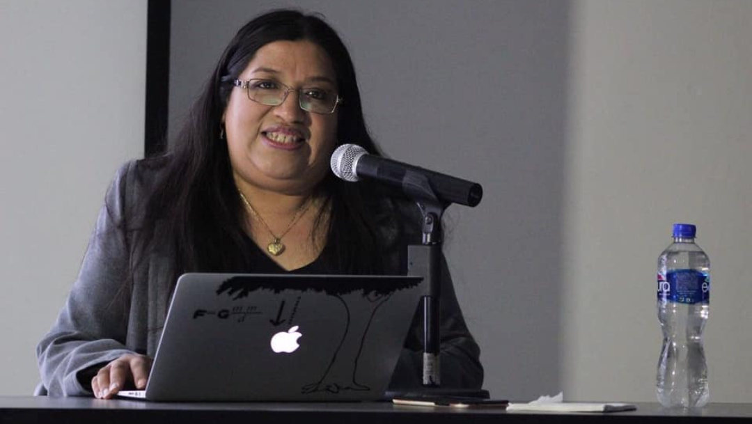mujer cabello negro y lentes frente a microfono y computadora