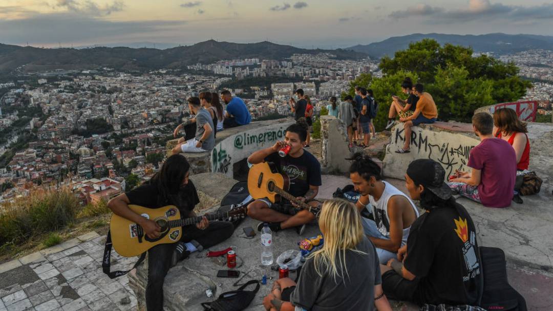 Un grupo de jóvenes toca la guitarra y comparte bebidas mientras disfruta una vista panorámica de Cataluña; autoridades temen que estas reuniones, conocidas como "botellón" sean foco de contagio de COVID-19