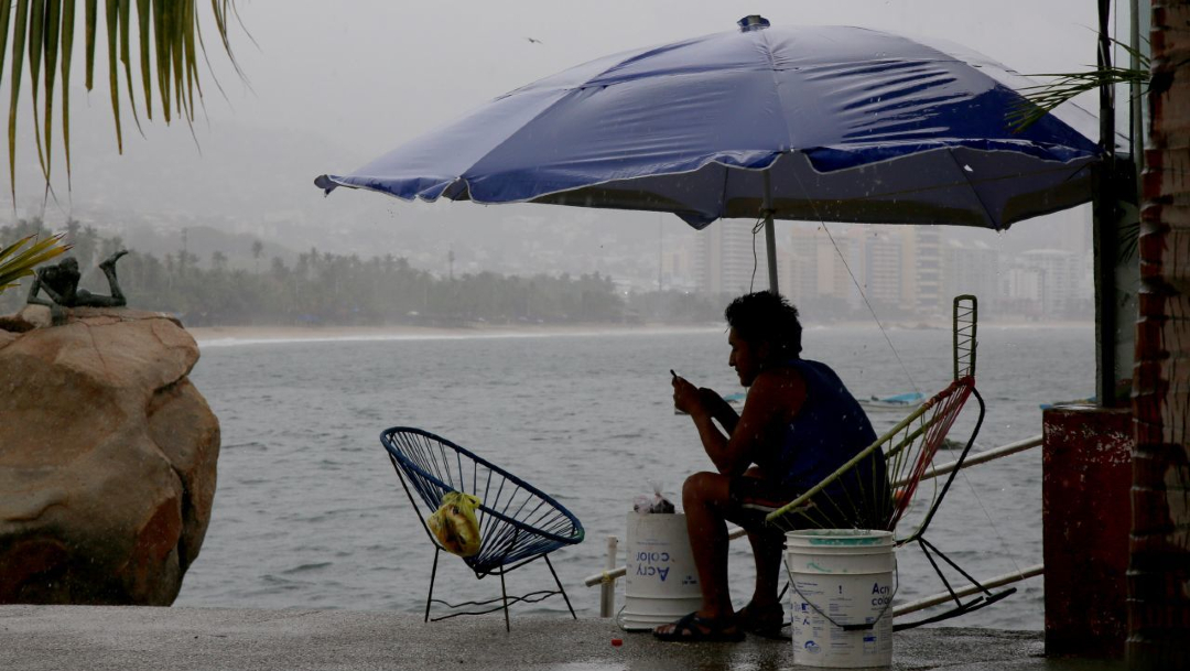 Un joven se resguarda bajo paragüas de la lluvia, frente al mar