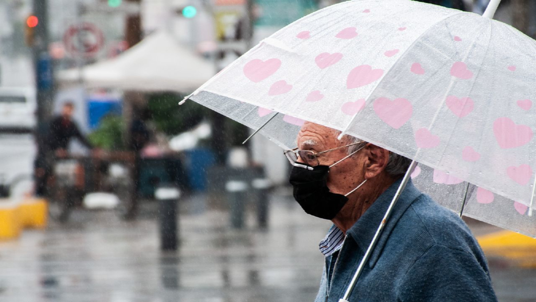 Un hombre de la tercera edad se cubre con un paragüas de la lluvia