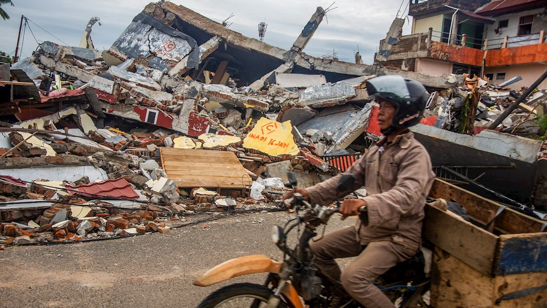 Un hombre conduce su motocicleta junto a casas derrumbadas tras un terremoto en Indonesia