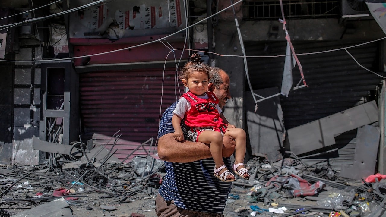 Un palestino lleva a su hija junto a una torre destruida, después de los ataques aéreos israelíes en la ciudad de Gaza, 18 de mayo de 2021 (EFE)