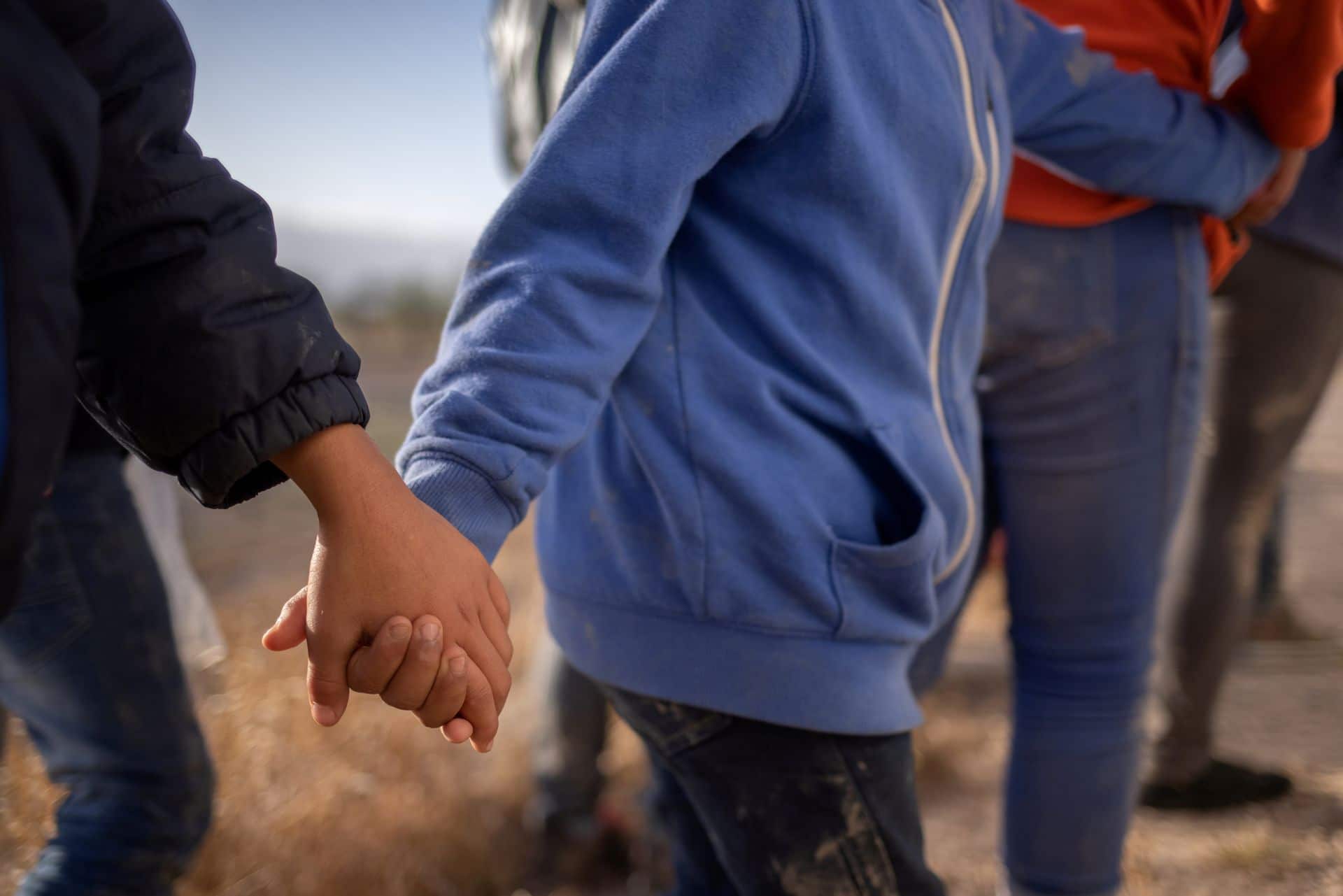 Los menores no acompañados solicitantes de asilo se toman de la mano en medio de migrantes adultos de Centroamérica (Reuters)
