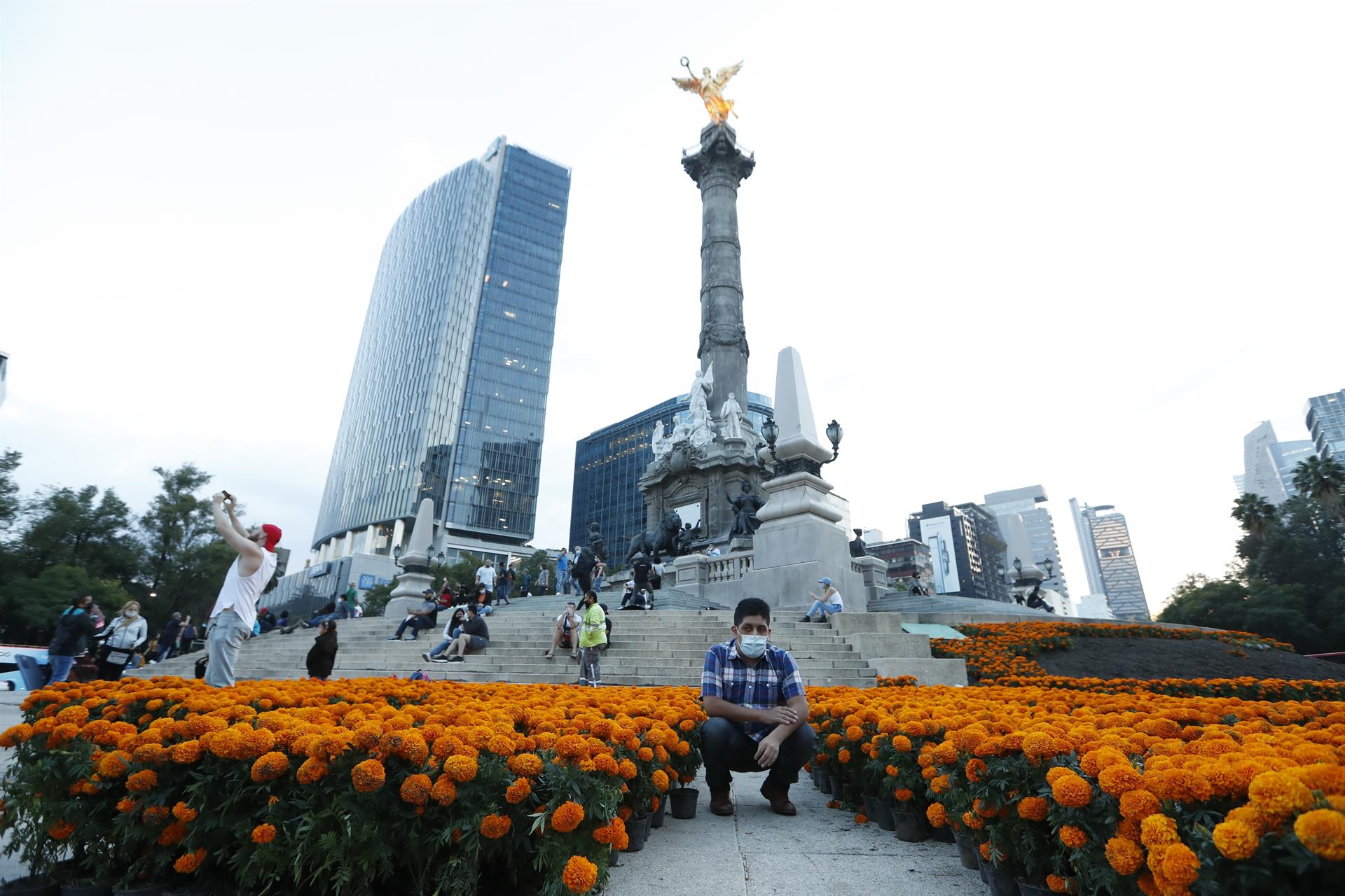 Un hombre se toma una fotografía con las flores de cempasúchil colocadas en el monumento del Angel de la Independencia (EFE)