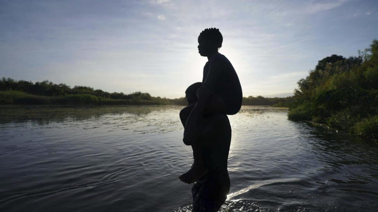 Un hombre carga a su hija al cruzar el río Bravo de Ciudad Acuña a Del Río, Texas (AP)