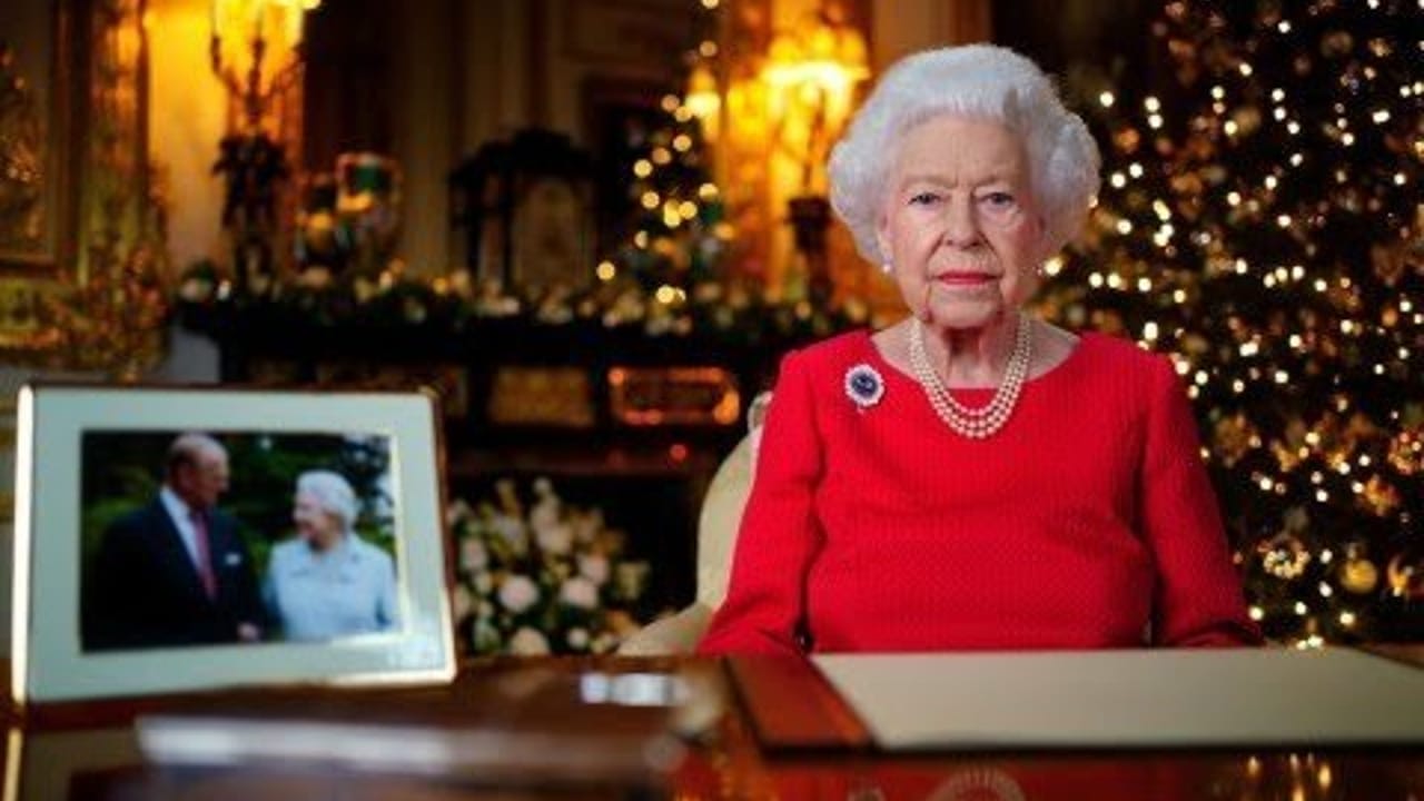 La reina Isabel II aparece en el video vestida de rojo, con una fotografía de ella y el duque sobre la mesa.
