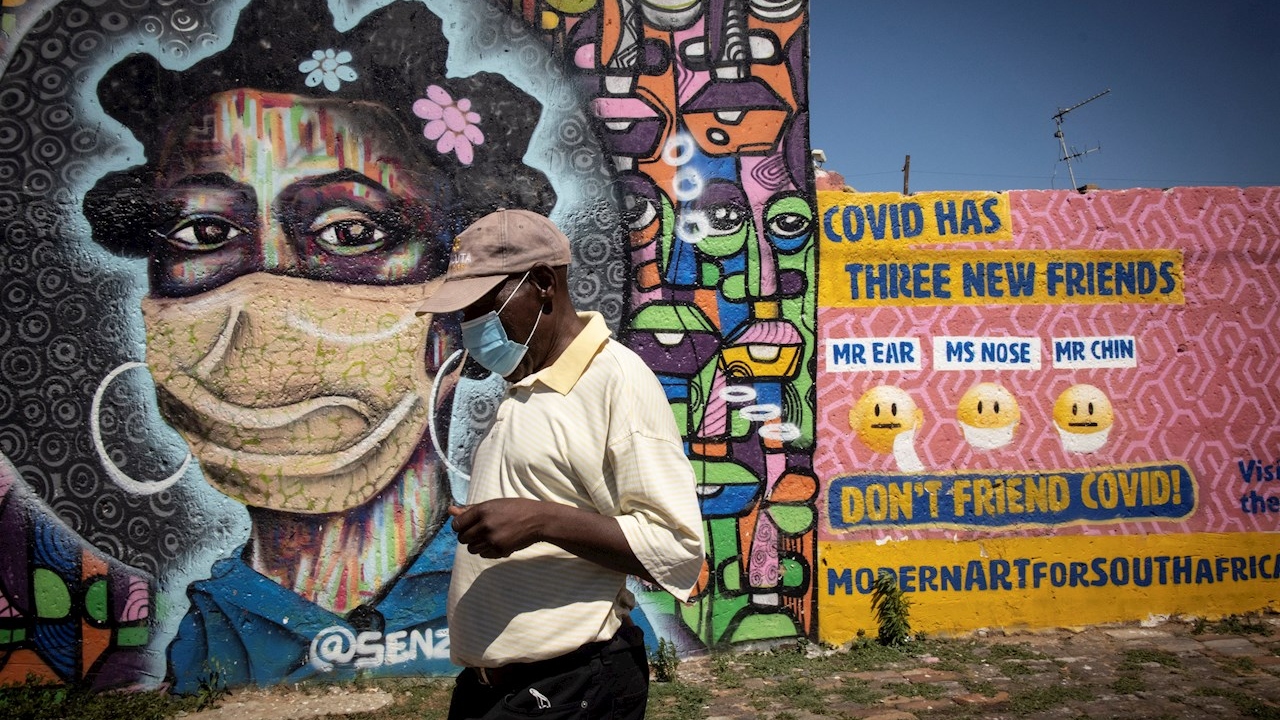Un ciudadano de Soweto, Sudafrica, camina frente a un graffiti informativo que educa a los residentes locales sobre los peligros del covid