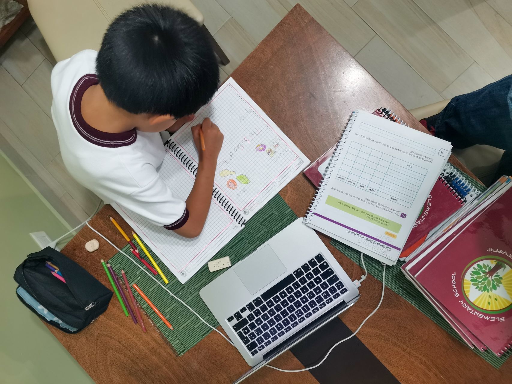 Un alumno de primaria a mitad de su jornada educativa, acompañado de su computadora y sus útiles escolares