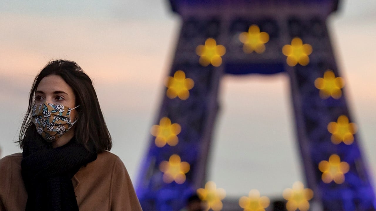 Una mujer usa su cubrebocas frente a la Torre Eiffel en París.