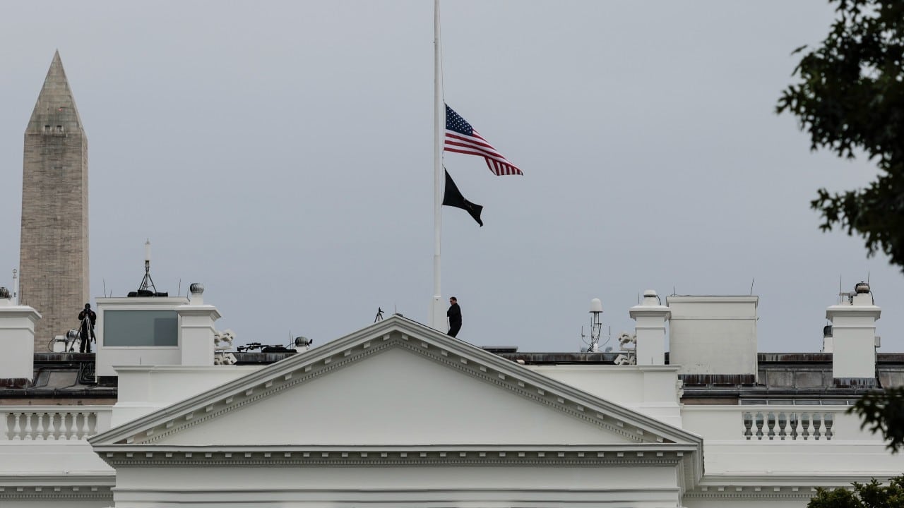 Un oficial del Servicio Secreto de EEUU baja la bandera estadounidense a media asta sobre la Casa Blanca tras el tiroteo masivo en una escuela primaria de Texas el 24 de mayo de 2022 (Getty Images)