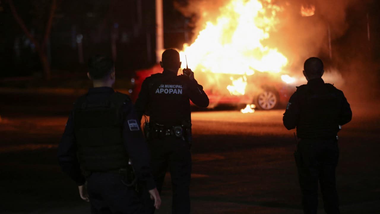 Agentes se paran en una escena donde miembros del Cártel Jalisco Nueva Generación (CJNG) incendiaron un vehículo tras la detención de uno de sus líderes en Zapopan, Jalisco (Reuters)