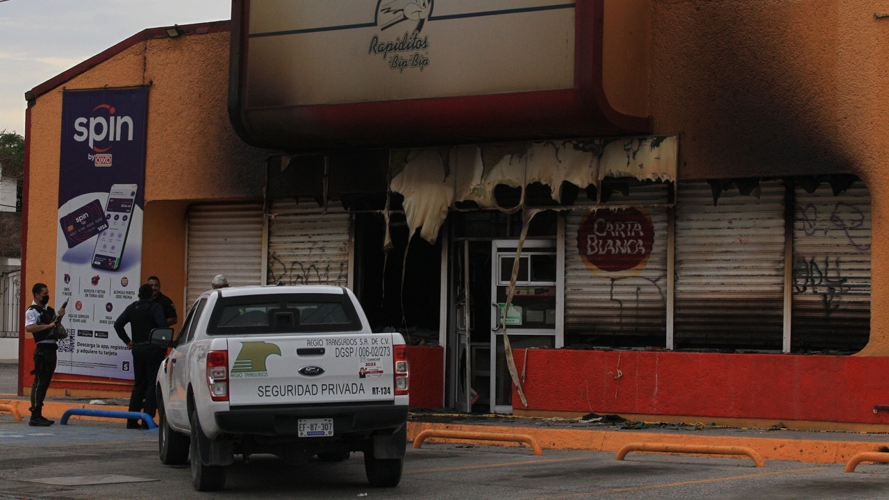 Policías estatales y de seguridad privada vigilan una tienda que fue incendiada por personas armadas en Ciudad Juárez