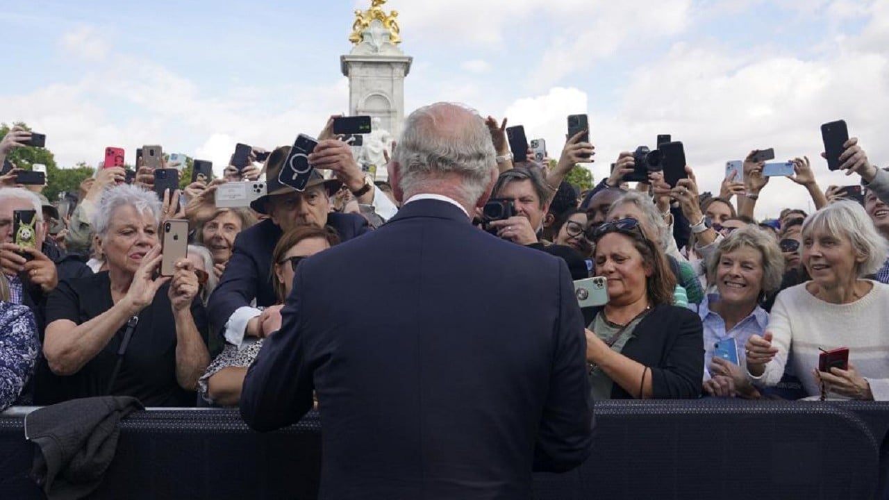 El rey Carlos III de Gran Bretaña, de espaldas a la cámara, saluda a los simpatizantes mientras camina por las puertas del Palacio de Buckingham (AP)